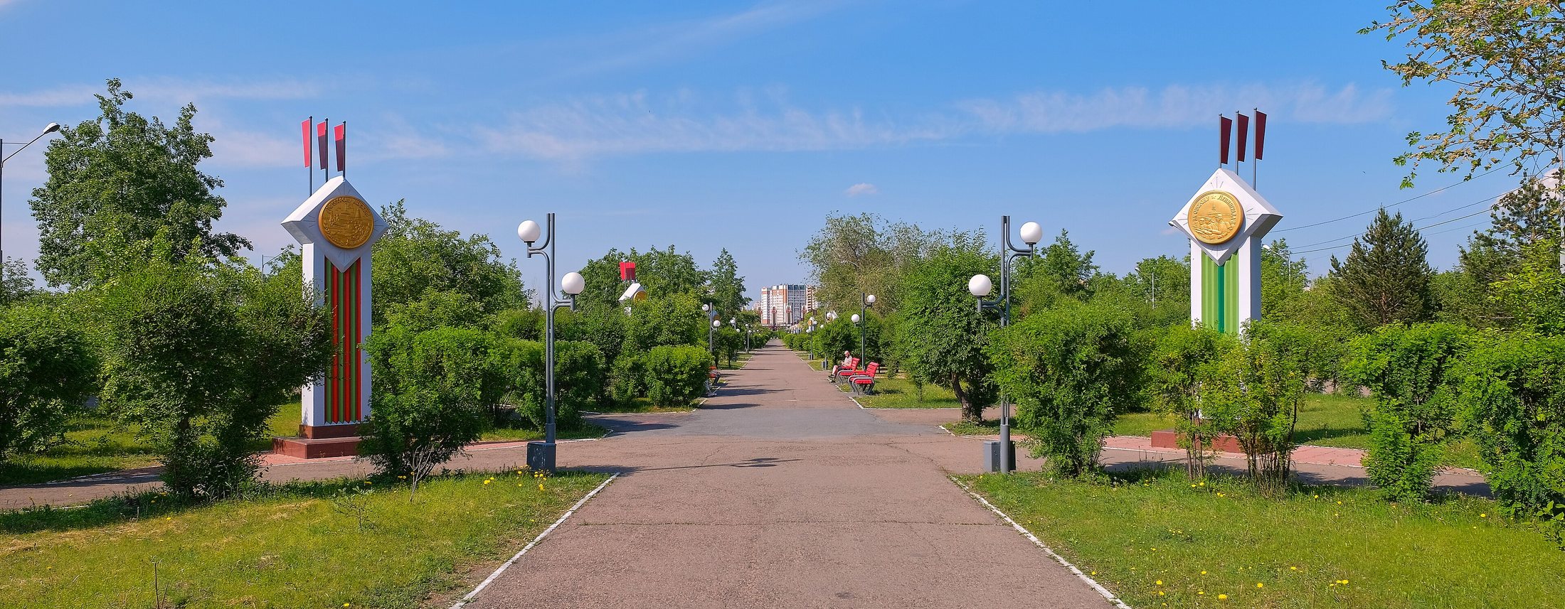 Центральная аллея сейчас: асфальт, разросшиеся кусты, две стелы с медалями